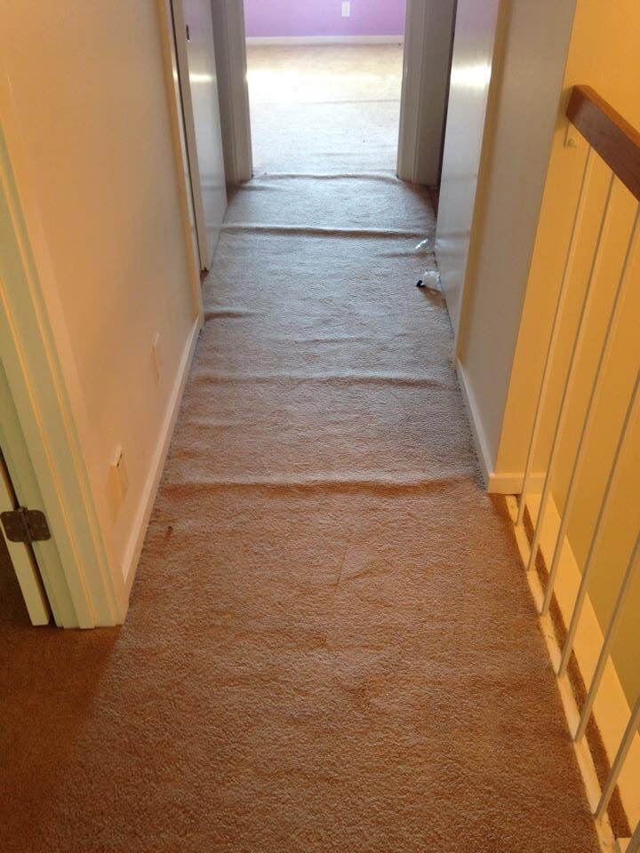 Hallway carpet with ripples and a visible crease line before restretching