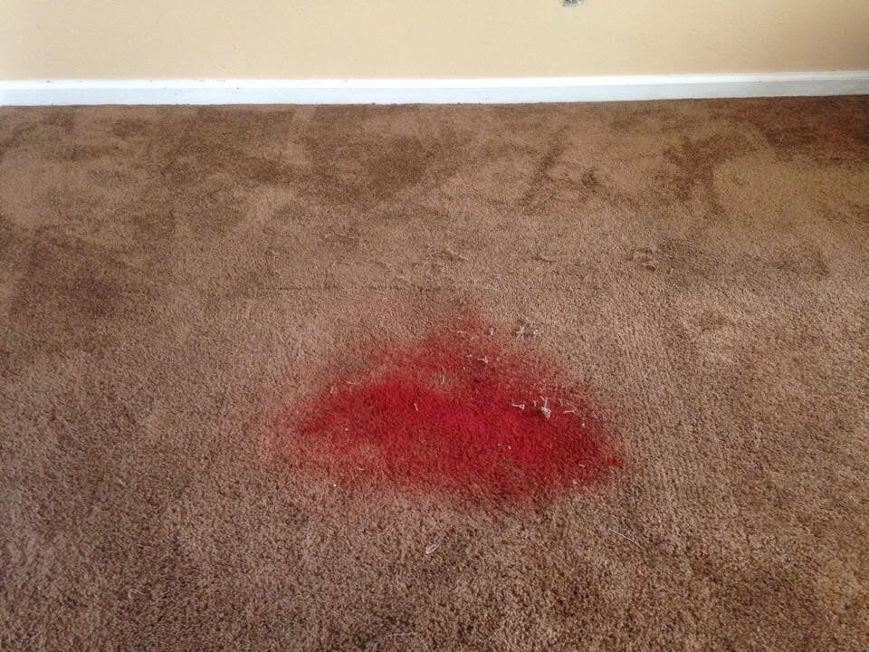 Large red stain on brown carpet before the damaged area was patched